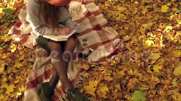 美丽的女人坐在秋天森林的格子上在笔记本上做笔记享受好天气慢动作视频的预览图