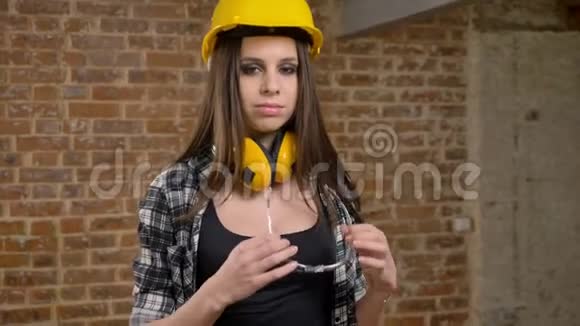 戴着头盔和耳机的漂亮可爱的年轻女性直视镜头戴上眼镜女建筑工人视频的预览图