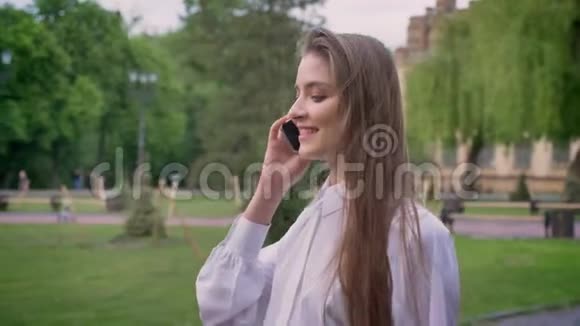 年轻漂亮的快乐女孩在夏天白天打电话去公园沟通观念视频的预览图