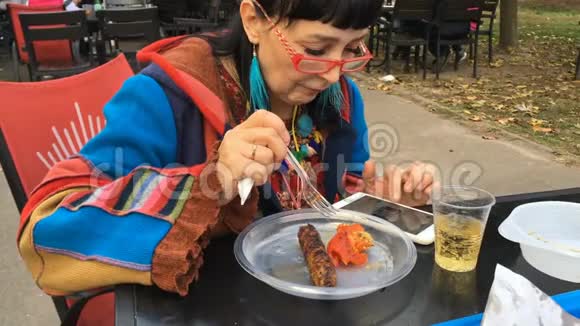 优雅的女人穿着时髦的衣服和红色的眼镜在户外咖啡馆吃肉视频的预览图