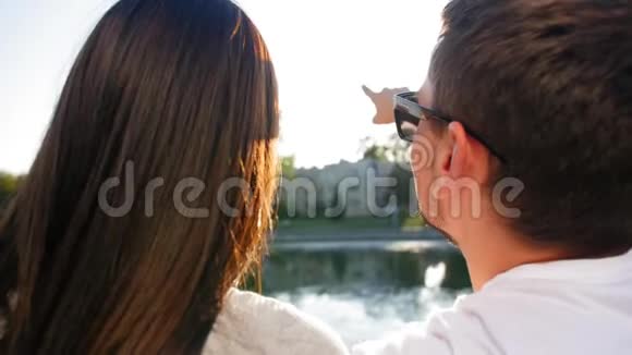 日落时分一对浪漫的情侣坐在池塘边的绿草上聊天后视图夫妻信任爱情和视频的预览图