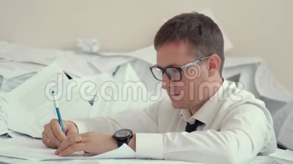 一个戴眼镜的疲惫的年轻人坐在一堆文件和签名文件里他手臂上有几个小时他累了视频的预览图