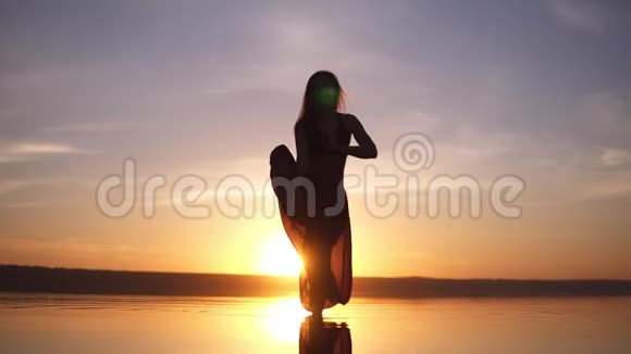 在美丽的夕阳下在海上海岸练习瑜伽姿势的剪影瑜伽女人一个穿瑜伽裤的女人视频的预览图