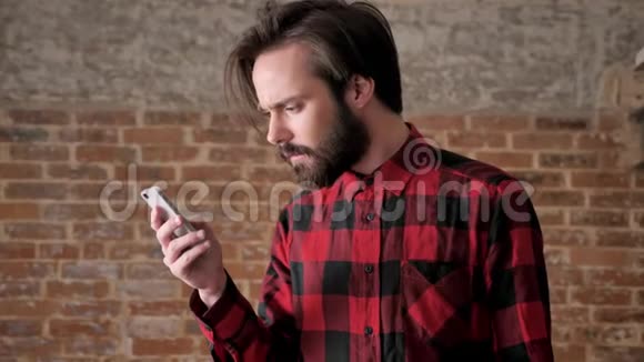 有胡子的年轻帅哥在智能手机上读信息通信概念砖背景视频的预览图