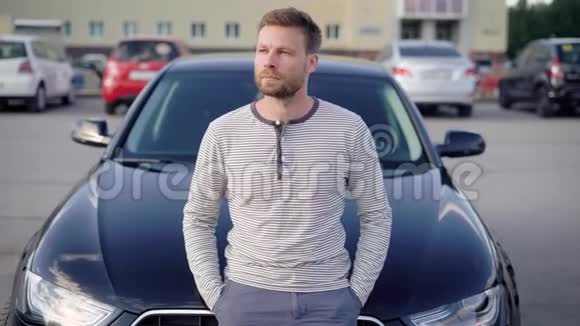 一个留着胡子的帅哥站在停车场他的车旁边他很体贴看着远处有人视频的预览图