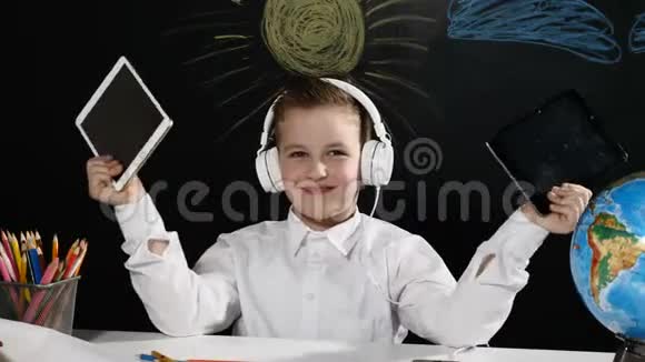 学校观念可爱的男孩坐在桌子上上面有地球仪还有他身后的黑板耳机里的积极学生视频的预览图