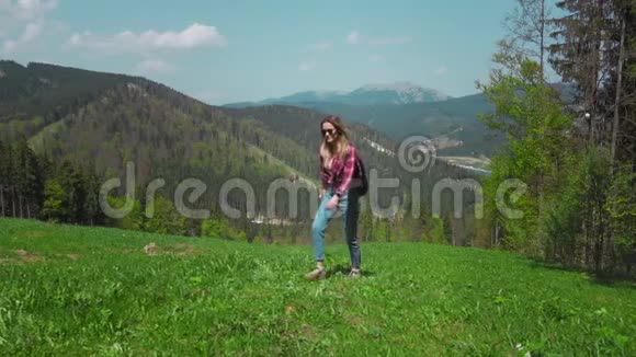 一个年轻的白人女人带着背包和太阳镜站在山上拿起她的手的概念视频的预览图