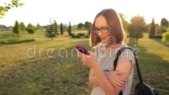戴眼镜聊天的休闲女孩使用智能手机傍晚的阳光灿烂视频的预览图