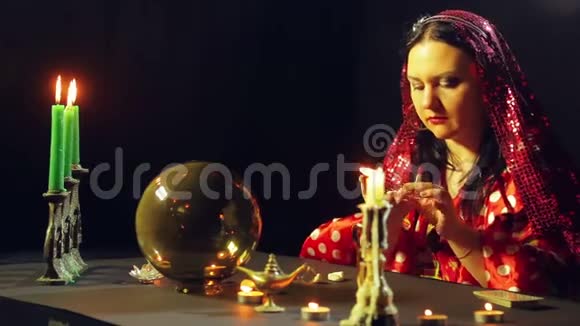 一个年轻的吉普赛人穿着红色的裙子在烛光下的桌子上读着石头上的未来平均计划视频的预览图
