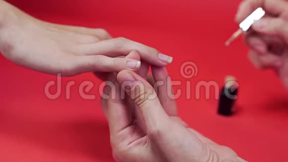 摩尼教客户的指甲用米色涂指甲油涂在红色背景化妆品和指甲上并将指甲贴紧视频的预览图