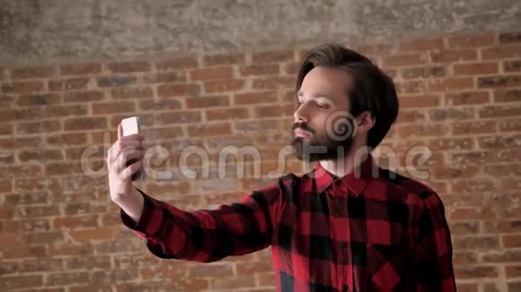 有胡子的年轻帅哥在智能手机上自拍沟通概念砖背景视频的预览图