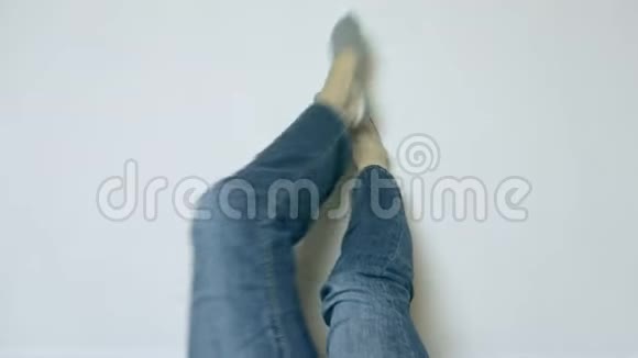 穿着牛仔裤和袜子的女人的双腿靠在白色的墙上放松有复印空间视频的预览图