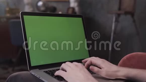 一个男人坐在他的桌子上在一台带有绿色屏幕的笔记本电脑上工作他的肩膀上的景色库存录像使用人类视频的预览图