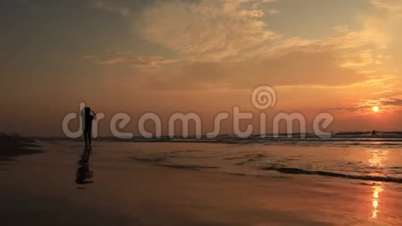 在沙滩上玩飞盘的剪影人们被夏日的阳光照得背光视频的预览图