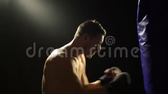 拳击概念一个拳击手在一个蓝色的梨子上训练孤立在黑色的背景上黑色背景的强壮拳击手视频的预览图