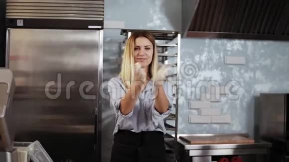 烹饪糕点的概念一位金发女子糖果师站在工作桌前嬉戏鼓掌的画像视频的预览图
