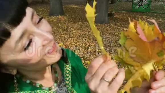 美丽幸福的女人穿着绿色的裙子在秋天的公园里分拣和玩黄色的叶子视频的预览图