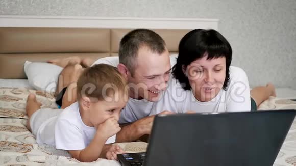 幸福家庭爸爸妈妈和宝宝躺在床上看着笔记本电脑笑嘻嘻视频的预览图