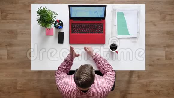 戴眼镜的年轻人通过笔记本电脑顶镜头咖啡和文件坐在办公桌后与人交谈视频的预览图