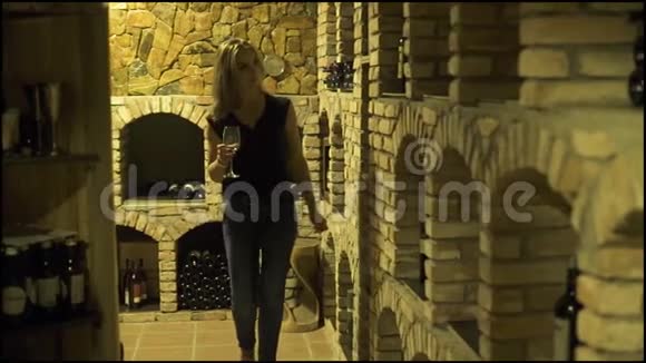 带着红酒酒杯的年轻女人在地窖里看着瓶子女子酿酒师在传统酒窖品尝红酒视频的预览图