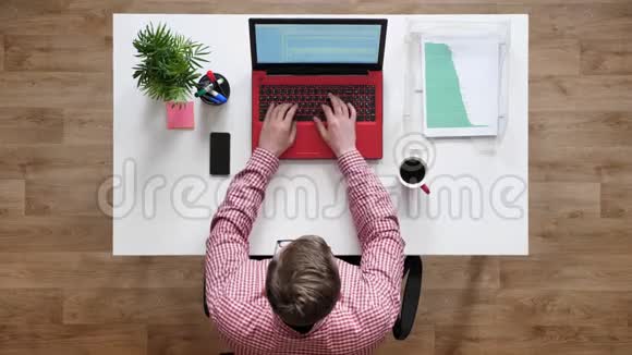 戴眼镜的年轻人在笔记本电脑上打字拿起电话顶头坐在桌子后面拿着咖啡和文件视频的预览图