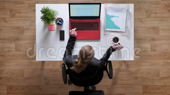 年轻女子扎着马尾辫在笔记本电脑上打字喝着咖啡坐在桌子后面拿着文件视频的预览图