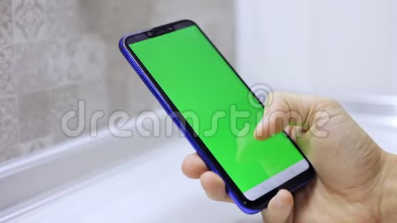特写男性手拿智能手机与绿色屏幕预键效果在屏幕上滚动和键入视频的预览图
