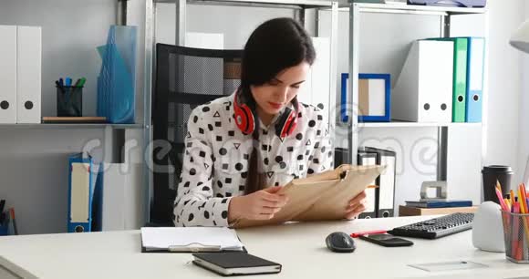 现代办公室里戴着红色耳机的女人用铅笔在纸上写字视频的预览图