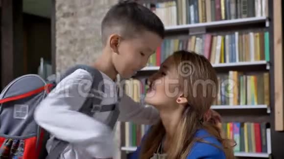 年轻的亚洲妇女带着背包送她的小儿子上学亲吻微笑书架和砖墙视频的预览图