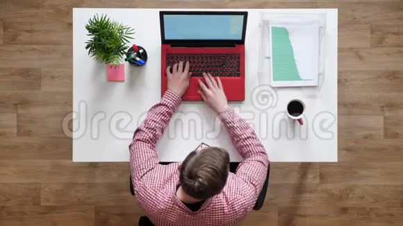 戴眼镜的年轻人在笔记本电脑上打字喝咖啡坐在桌子后面拿着文件视频的预览图