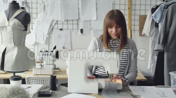 年轻有魅力的裁缝师在缝纫机上工作在她的工作室里看着女人服装草图视频的预览图