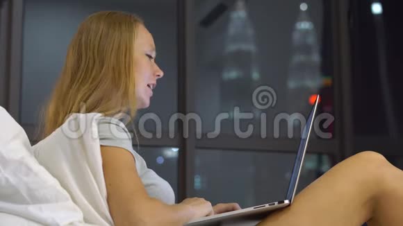 一位年轻女子在床上坐着一台笔记本电脑一边聊天一边唱歌一边剪影着摩天轮视频的预览图