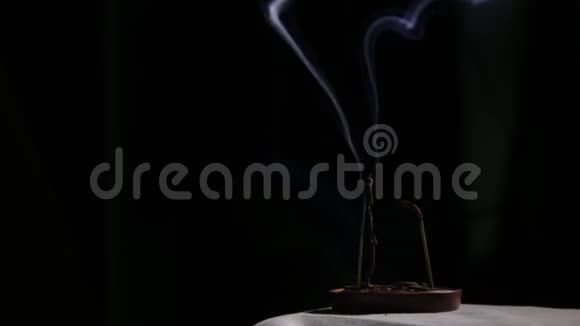 燃烧着的香棒蓝色的烟雾在黑暗的背景上缓缓流动视频的预览图