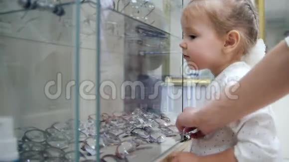 商店里的小女孩选择眼镜孩子把手指放在什么东西上妈妈允许买它视频的预览图