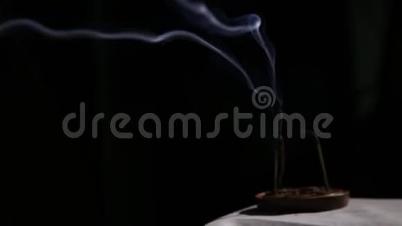 燃烧着的香棒蓝色的烟雾在黑暗的背景上缓缓流动视频的预览图