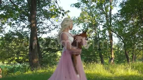 女孩抱着一只狐狸朝她微笑它就在盛开的树木附近在春天的公园里视频的预览图