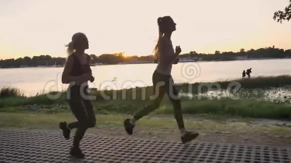 两个年轻漂亮的女人在公园里在河边的桥上跑步日落时分减肥健身模特慢跑视频的预览图