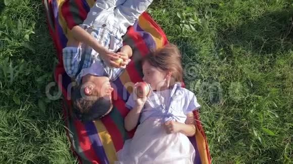 健康的孩子咬苹果躺在草地上的毯子上视频的预览图