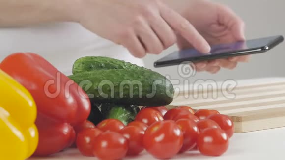 女人选择蔬菜做沙拉看智能手机屏幕上的食谱视频的预览图