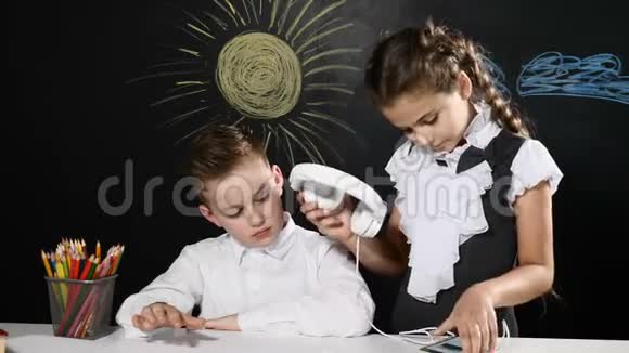 学校理念可爱的男孩和漂亮的女孩坐在书桌旁身后是黑板女学生给男孩戴上耳机视频的预览图