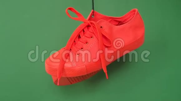 一双红色运动鞋挂在绿色背景上橙色的靴子挂在绳子上视频的预览图