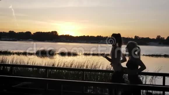 日落时分两个扎着马尾辫的年轻女人在河边公园里奔跑美丽的风景减肥健身模特视频的预览图