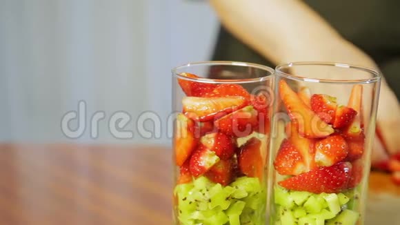 一个女人把碎奇异果片的成熟草莓放进玻璃杯里视频的预览图