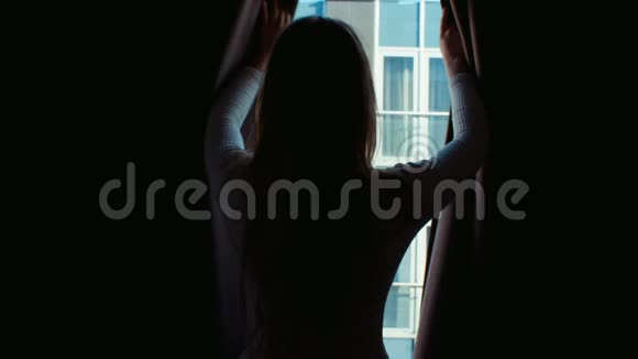 年轻女人的剪影打开窗帘望着窗外视频的预览图