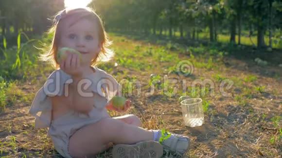 小女孩玩得很开心小可爱的女孩手里拿着水果坐在花园的两排草地上视频的预览图