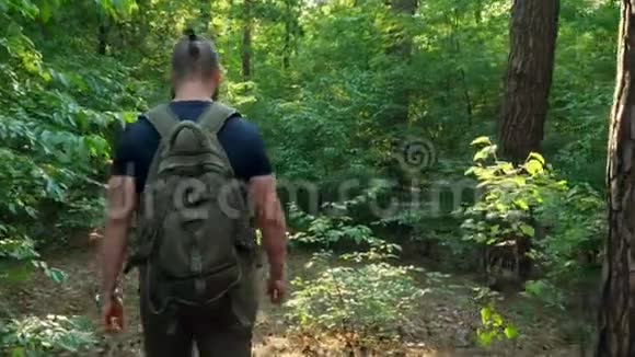一个带背包的留胡子的人穿过森林摄像机跟着他移动自然旅途旅行视频的预览图