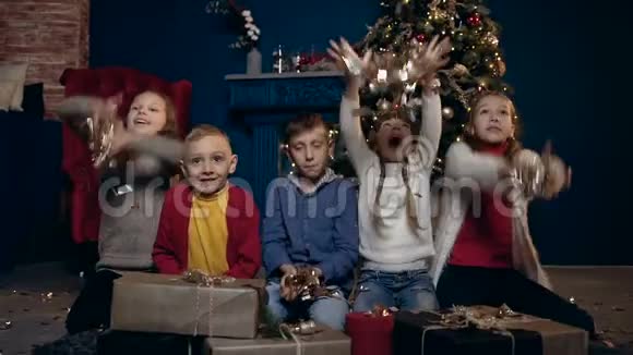 可爱的快乐儿童坐在圣诞树附近带着礼物开始扔纸屑视频的预览图