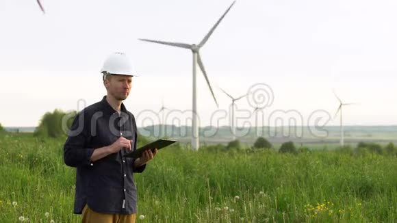 工人站在白色风力涡轮机附近在平板电脑上打字风车绿色能源理念视频的预览图