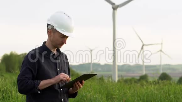 工人站在白色风力涡轮机附近在平板电脑上打字风车绿色能源概念视频的预览图