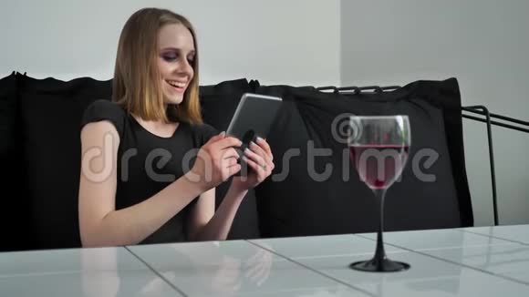 年轻迷人的女人用平板电脑化妆坐在沙发上笑着黑白咖啡背景视频的预览图